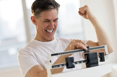 Chiropractic Phoenix AZ Weight Loss BOX A man celebrating results while he weighs himself on a scale